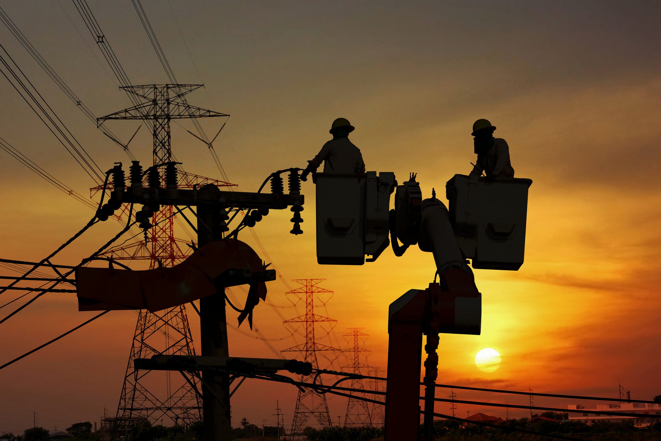 Workers on power lines at sunset.